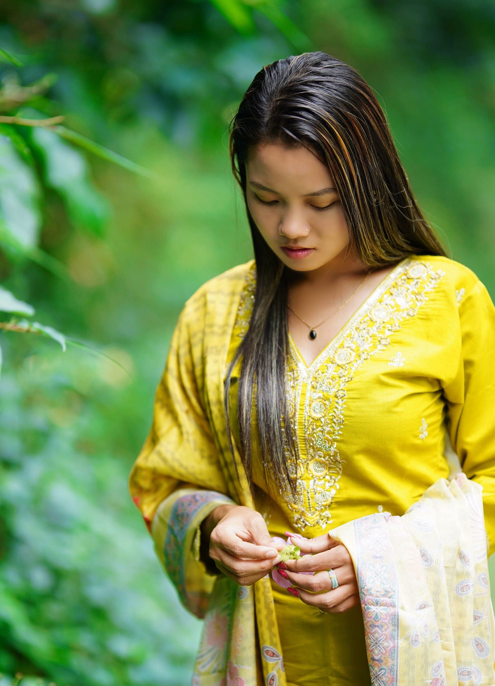 Woman in a yellow lightly embroidered lawn kameez with a printed dupatta, standing in greenery