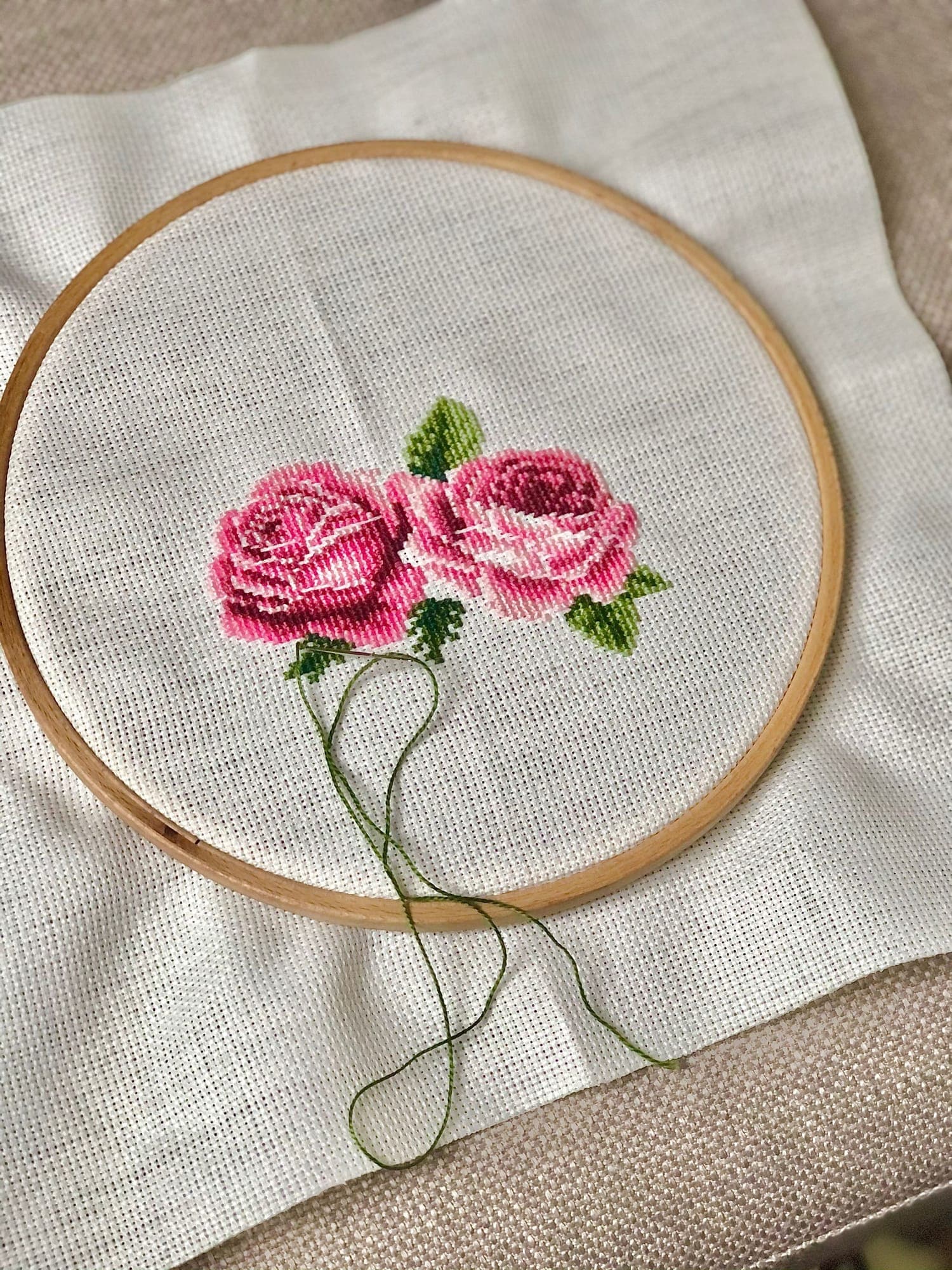 Pink cross-stitch roses in a wooden hoop on white linen in soft daylight