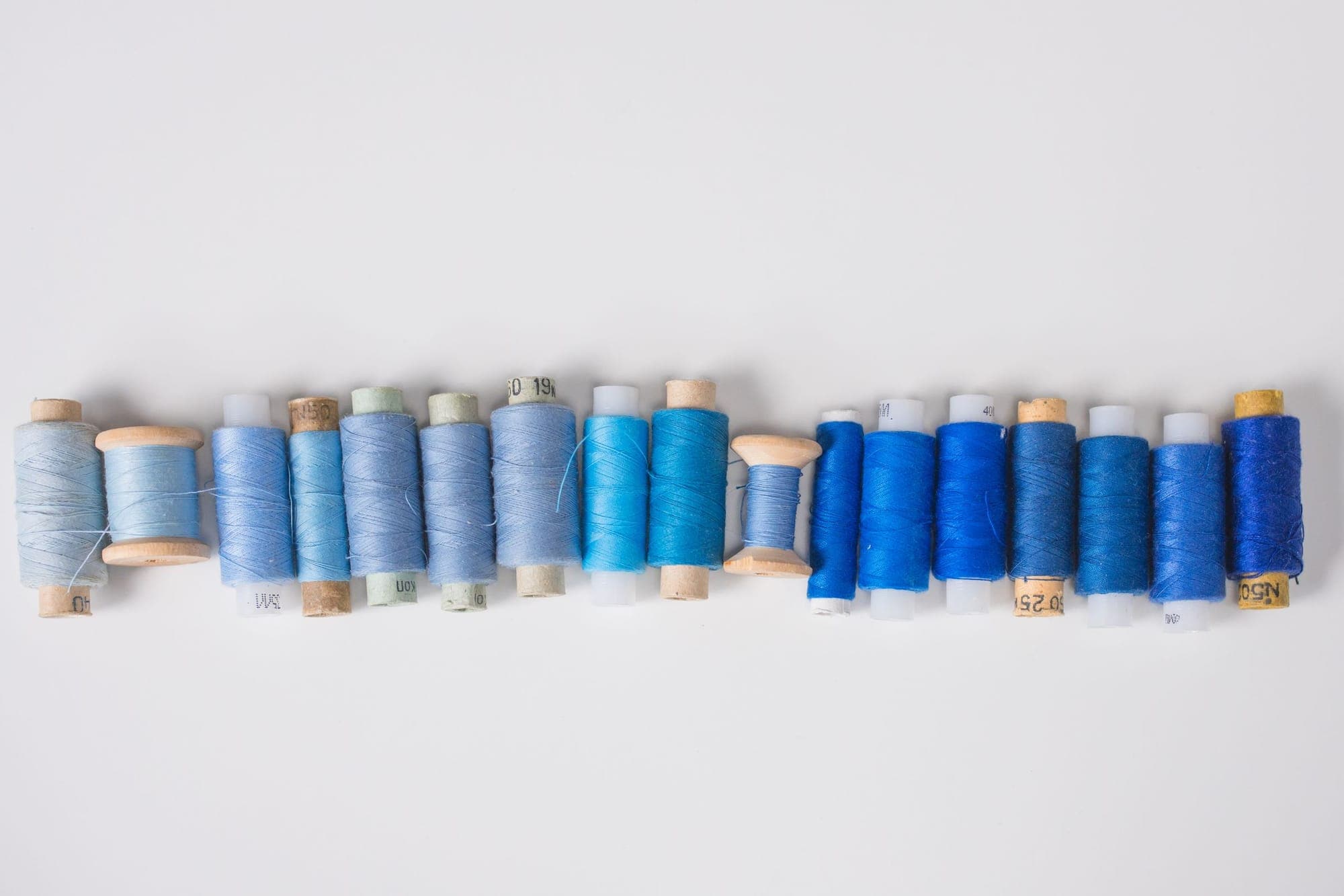 A row of blue thread spools arranged on a white surface
